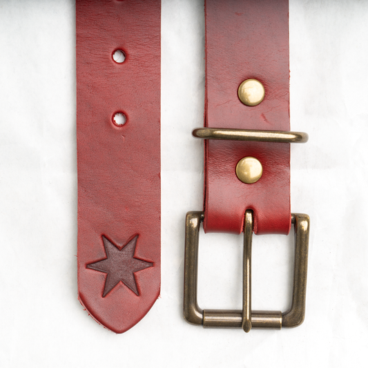 Red leather belt with antique brass buckle, laid flat and coiled